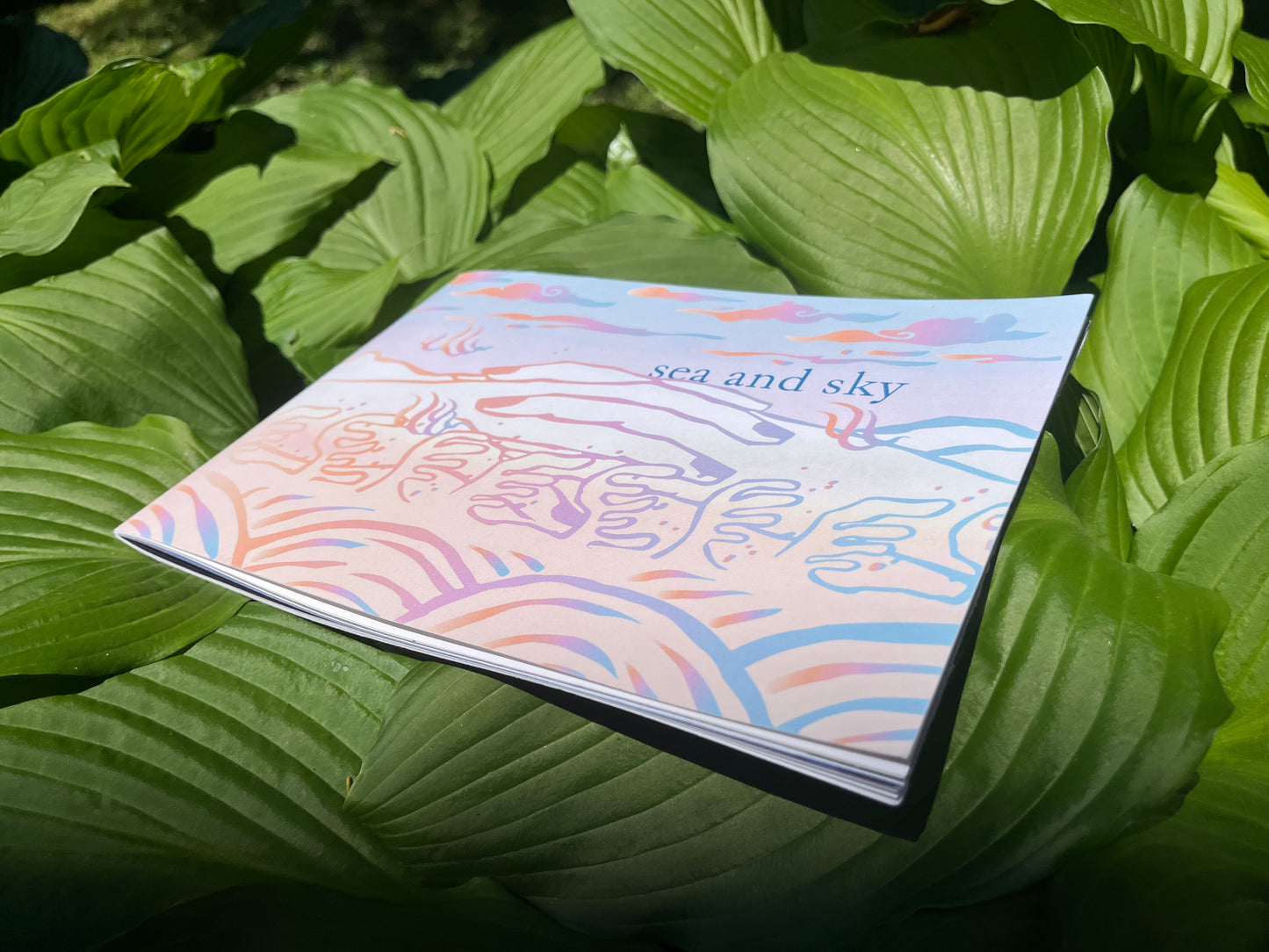 sea and sky zine cover. Hands join together in a landscape of clouds, mountains, and water in pastel gradient. sea and sky zine is about community found through dreams and the fold over of past, present, and future.