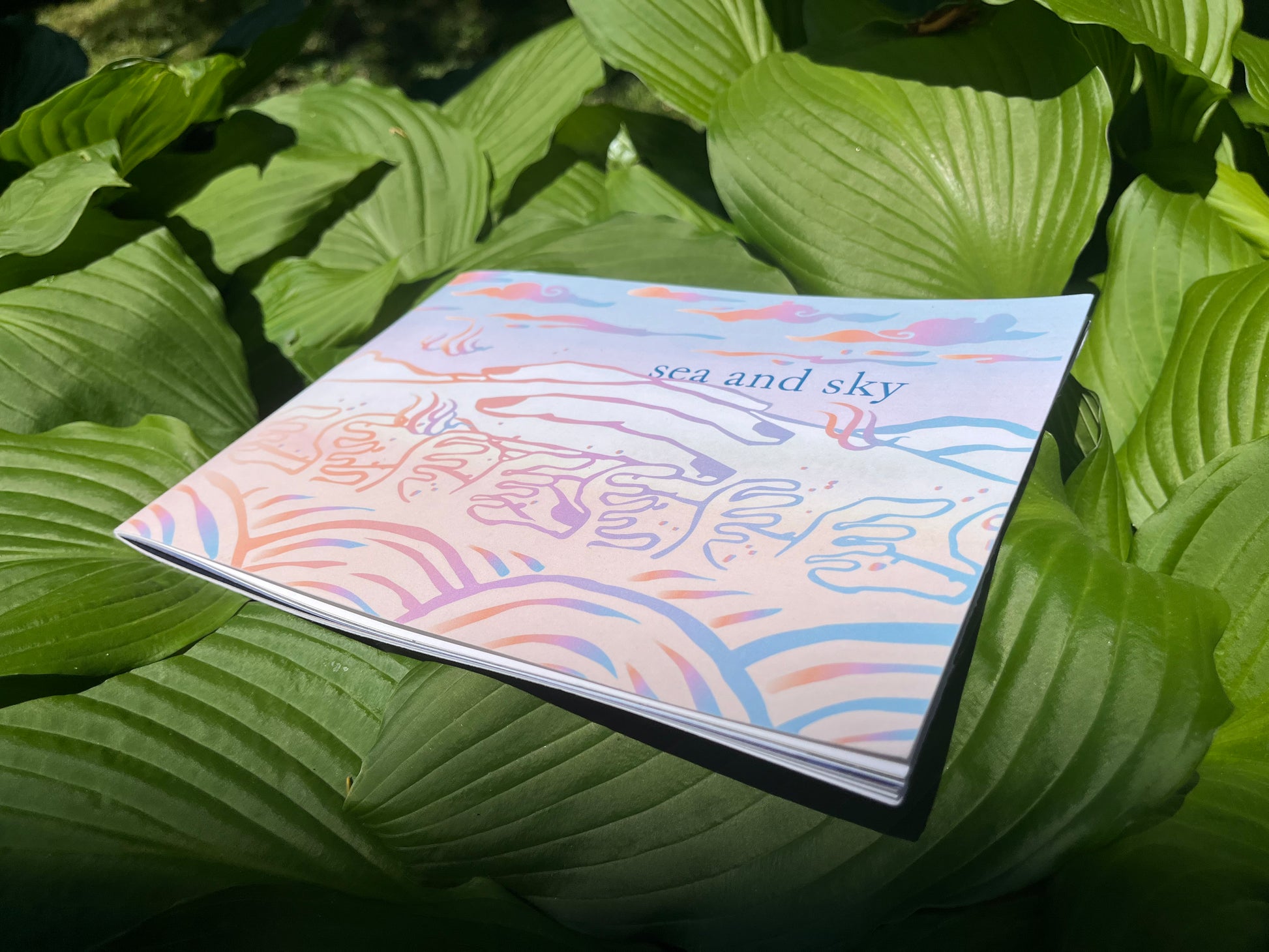 sea and sky zine cover. Hands join together in a landscape of clouds, mountains, and water in pastel gradient. sea and sky zine is about community found through dreams and the fold over of past, present, and future.