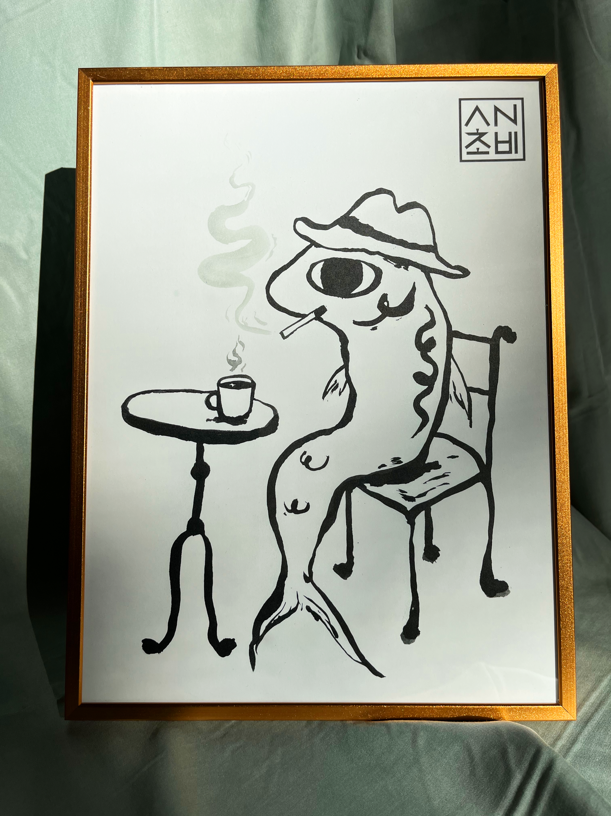 9x12 Matte Finish Black and White Art Print for home, apartment, and room decor. Featured here in a gold frame. Anchovy Studio design original print by independent artists. Inspired by calligraphy and expressionism. In this artwork, an anchovy smokes a cigarette with a cup of coffee, head full of thoughts.