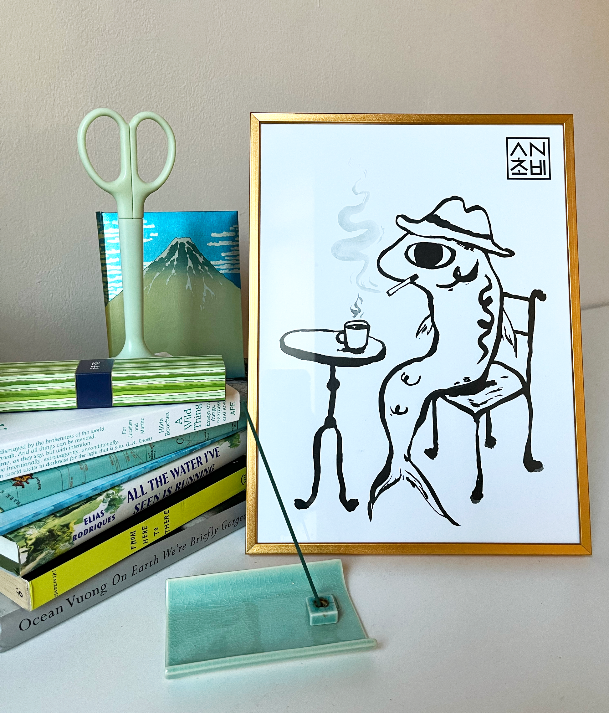 9x12 Matte Finish Black and White Art Print for home, apartment, and room decor. Featured here in a gold frame. Anchovy Studio design original print by independent artists. Inspired by calligraphy and expressionism. In this artwork, an anchovy smokes a cigarette with a cup of coffee, head full of thoughts.