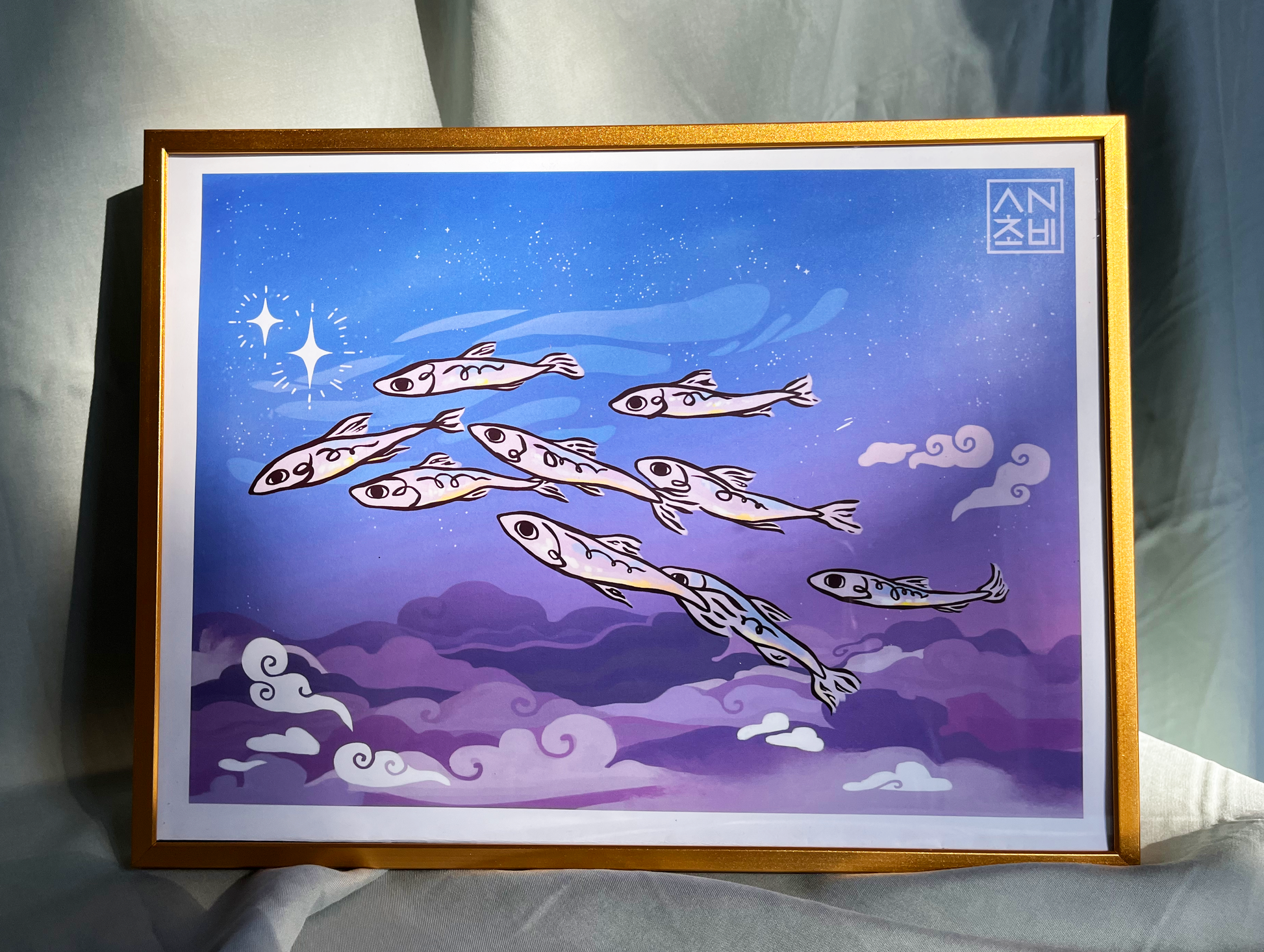 9x12 Gloss Finish Color Art Print in full color for home, apartment, or room decor. A school of anchovies flies together in the evening sky among blue and purple clouds and stars. Anchovy Studio original design by independent artists. Featured here in a gold frame.